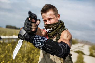 portrait of a vandal man with a gun and dirty clothes against the backdrop of an abandoned bridge