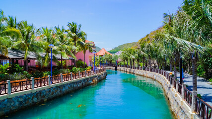 A man-made canal with alleys of palm trees along the shore. A sunny summer day. Vinpearl Island in...