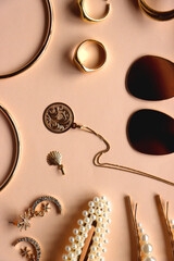 Various gold jewelry and pearl hair clips on peach colored background. Flat lay.