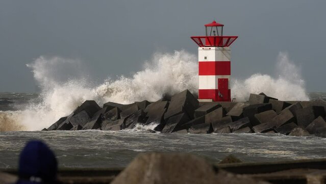 Rough sea breaks over jettty and lighthouse on the coast of Scheveningen, The Hague, The Netherlands. Slow motion