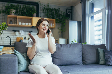 Pregnant beautiful woman sitting on the couch at home, talking on a cell phone with family, friends, colleagues. Has a good mood
