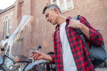 Man in a plaid red shirt standing near the street motobike