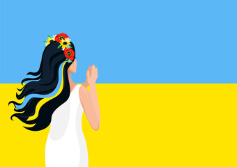 A young girl folded her hands to pray for Ukraine against the backdrop of the Ukrainian flag. Pray for Ukraine. Help and support for Ukraine. Stop the war.
