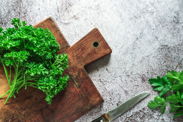 green fresh fragrant parsley with a knife for slicing greens lies on a wooden board on a gray background 2