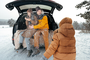 Lovely smiling couple sitting in car trunk in winter forest