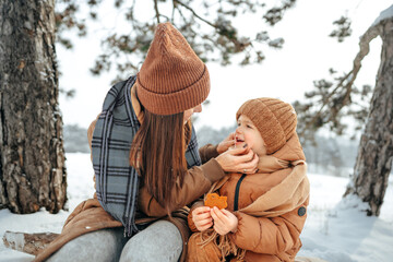 Young woman with a son in winter forest on a picnic drink hot tea