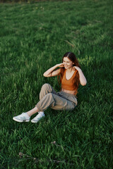 A woman enjoying the outdoors sitting in the park on the green grass in casual clothing with long flowing hair, lit by the bright summer sun without mosquitoes