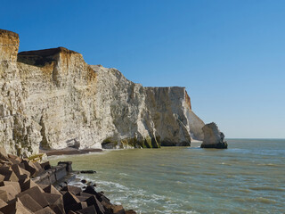 A coast of white cliffs - strata clearly visible - and a rock outcrop stack stand against gentle...