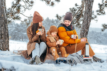 Fototapeta na wymiar Happy family with cups of hot tea spending time together in winter forest