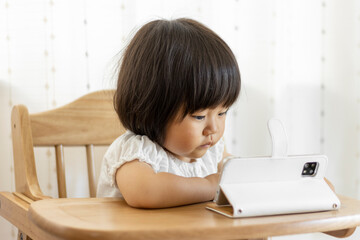 Naklejka premium 座ってスマートフォンで動画を見る赤ちゃん（1歳10か月、女の子、日本人）