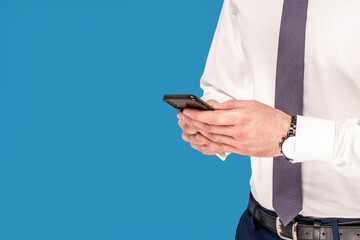 Closeup photo of men's hands holding mobile smart phone, touching screen, typing, studio shot isolated on blue background.