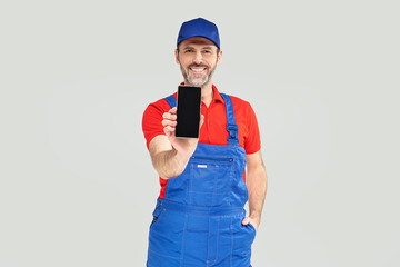 Smiling handsome plumber, repairman looking at camera, smiling and holding mobile phone with empty screen. Handyman.