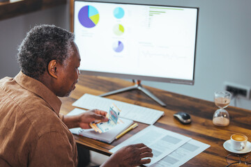 Stressed elderly grey-haired man in glasses look at laptop screen have problems paying bills taxes online. Thoughtful mature 70s male manage household finances, calculate expenses expenditures at home