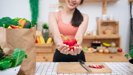 ํYoung woman is holding a large amount of radish fruit in her hand. by standing in the kitchen wearing sportswear.Vegan Vegetarian eat Salad Vitamin rich in nutrients.Organic vegetable for family.