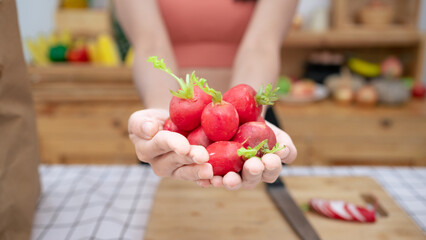 ํYoung woman is holding a large amount of radish fruit in her hand. by standing in the kitchen wearing sportswear.Vegan Vegetarian eat Salad Vitamin rich in nutrients.Organic vegetable for family.
