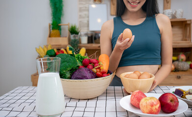 Young beautiful Asian woman holding organic fresh egg at home with surprise face.Woman taking eggs.Healthy food nutrition super food.Sport girl in yoga sport wear eat breakfast in home kitchen. 