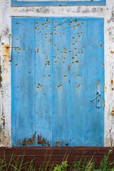 Old shabby wooden door, blue and white, with rusty hinges, a handle, a lock, and nails. Copy space. 