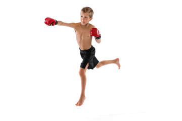 Punching. Little boy, kid in sports shots and gloves practicing thai boxing on white studio...