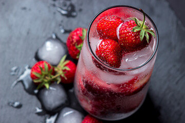 Cocktail with strawberries and ice on a black background. Refreshing drink.