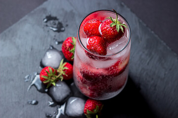 Cocktail with strawberries and ice on a black background. Refreshing drink.