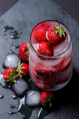 Cocktail with strawberries and ice on a black background. Refreshing drink.