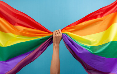 Man's hand holding colorful rainbow flag on blue color background. LGBT concept.