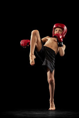 Studio shot of preschool boy, cute kid in sports shots and gloves training alone on black...