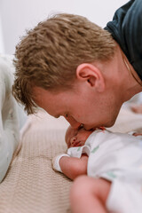 A father gently kisses a newborn baby lying in his crib