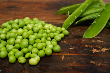 Fresh peeled green pease on a brown wooden table with copy space. Still life of green peas in pods with pea shoots on wooden table