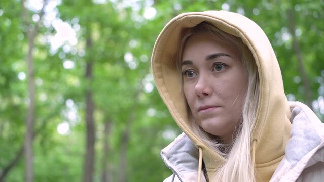 A young attractive Caucasian millennial woman looks thoughtfully into the distance in the forest. A woman in casual clothes with a hood leads a healthy and active lifestyle.