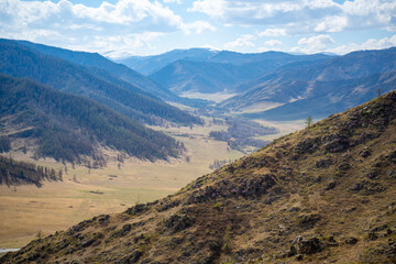 Scenic view from mountain pass to forest valley among mountain ranges and hills on horizon at changeable weather in spring time in Altai, Russia