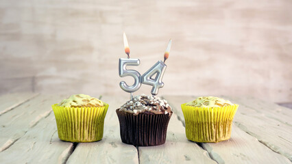 Happy birthday muffins with candles with the number 54. Card copy space with pies for...