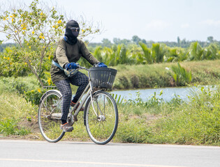 A masked woman rides a bicycle on a rural road