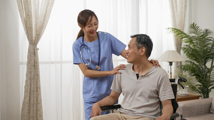 Asian female nurse and male senior wheelchair user enjoying chatting by the window at home. in-home social care for elderly disabled people concept