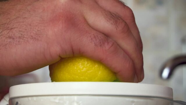 Man's hand squeezes juice from a lemon. Juicer work. Yellow fruit. Vitamin C. Juicing. Close-up. Kitchen in the house. Refreshing drink.