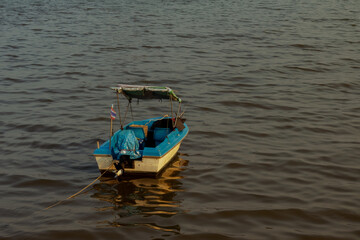 a small fishing boat floating on the sea with the sunset sunlight hitting the water surface