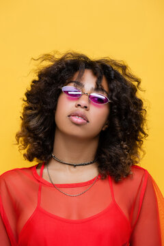 portrait of african american woman wearing fashionable sunglasses and necklaces isolated on yellow.