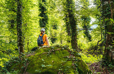 Rear view of young woman in yellow with backpack walking in summer forest next to green moss stone in summer active healthy lifestyle beauty in nature copy space