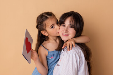 Happy little girl congratulating smiling mother and giving card with red heart