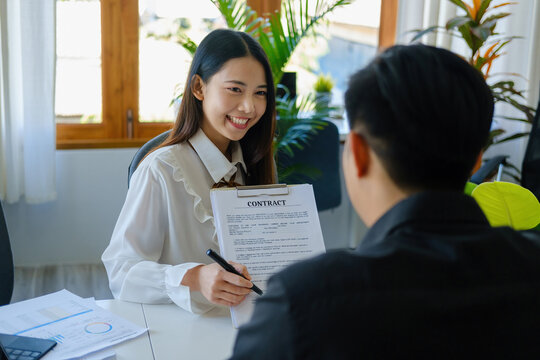 Guarantee, Mortgage, Signing, Insurance, Portrait of an agent or bank employee Asian woman holding important documents for male clients to read before signing an agreement