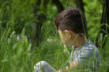 Naklejka na ściany i meble The boy sits in the grass grimaces, a warm summer evening