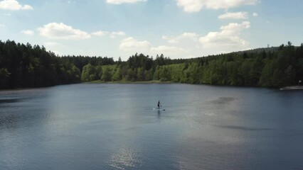 A lone person paddling a stand up paddleboard across a calm pond on vacation, aerial orbit