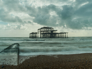The skeletal ruins of Brighton West Pier under a dramatic sky seen from the shingle beach; a slow...