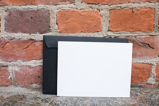 Mockup friendly template of postcard certificate with black envelope on a brick wall background