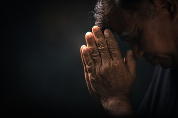 Elderly Asian man bowed his head praying to God on a black background at home. Holding hands in...