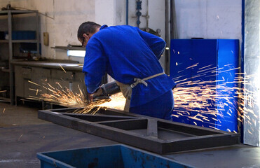 Employee of a metallurgical company using a grinder on a metal part.
The grinder is an electric tool used to cut, polish, sand and finish steel parts and metal structures in general.
