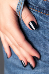 Female hand with beautiful manicure - dark black nails on jeans denim textile, closeup fingers. Selective focus