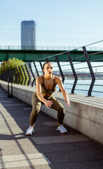 Fototapeta na wymiar Young woman in sportswear exercising on a river promenade