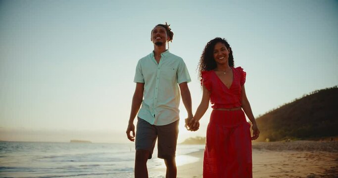 Beautiful young diverse black couple enjoying sunset walk on the beach on vacation