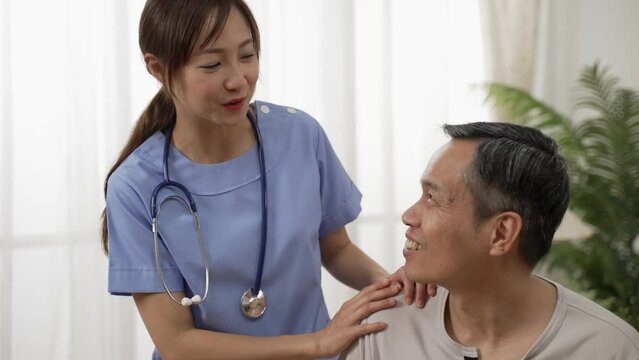 Closeup of caring Asian woman nursing aide talking and encouraging older male patient during home visit. Domiciliary care for elderly senior concept